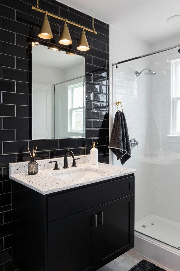 Bathroom interior with black subway tile walls, four gold cone pendant lights above a rectangular mirror, black vanity cabinet with white quartz countertop and matte black faucet, soap dispenser, reed diffuser, dark towel on gold hook, and clear glass shower enclosure with white tile interior.