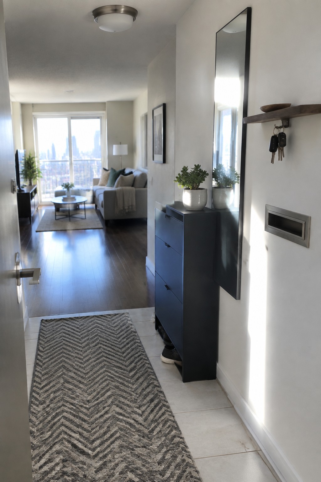 Modern hallway with chevron runner rug, blue cabinet, mirror, plants, and city-view living room