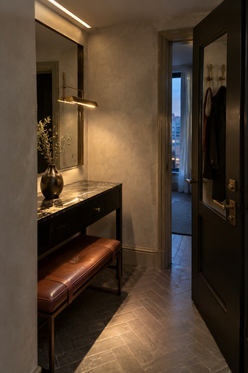 A narrow interior entryway with a dark console table topped in marble, a brown leather bench underneath, a large mirror on the wall, and a linear wall-mounted light fixture above the table.