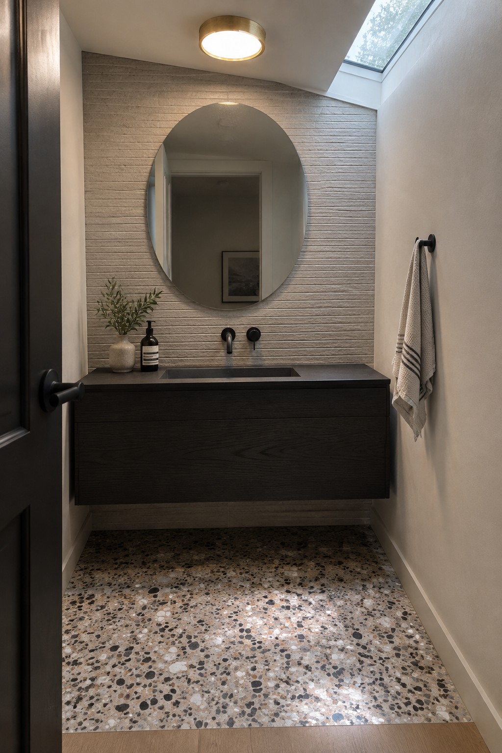 A small modern bathroom with a round flush mount ceiling light above a floating dark wood vanity and terrazzo floor.