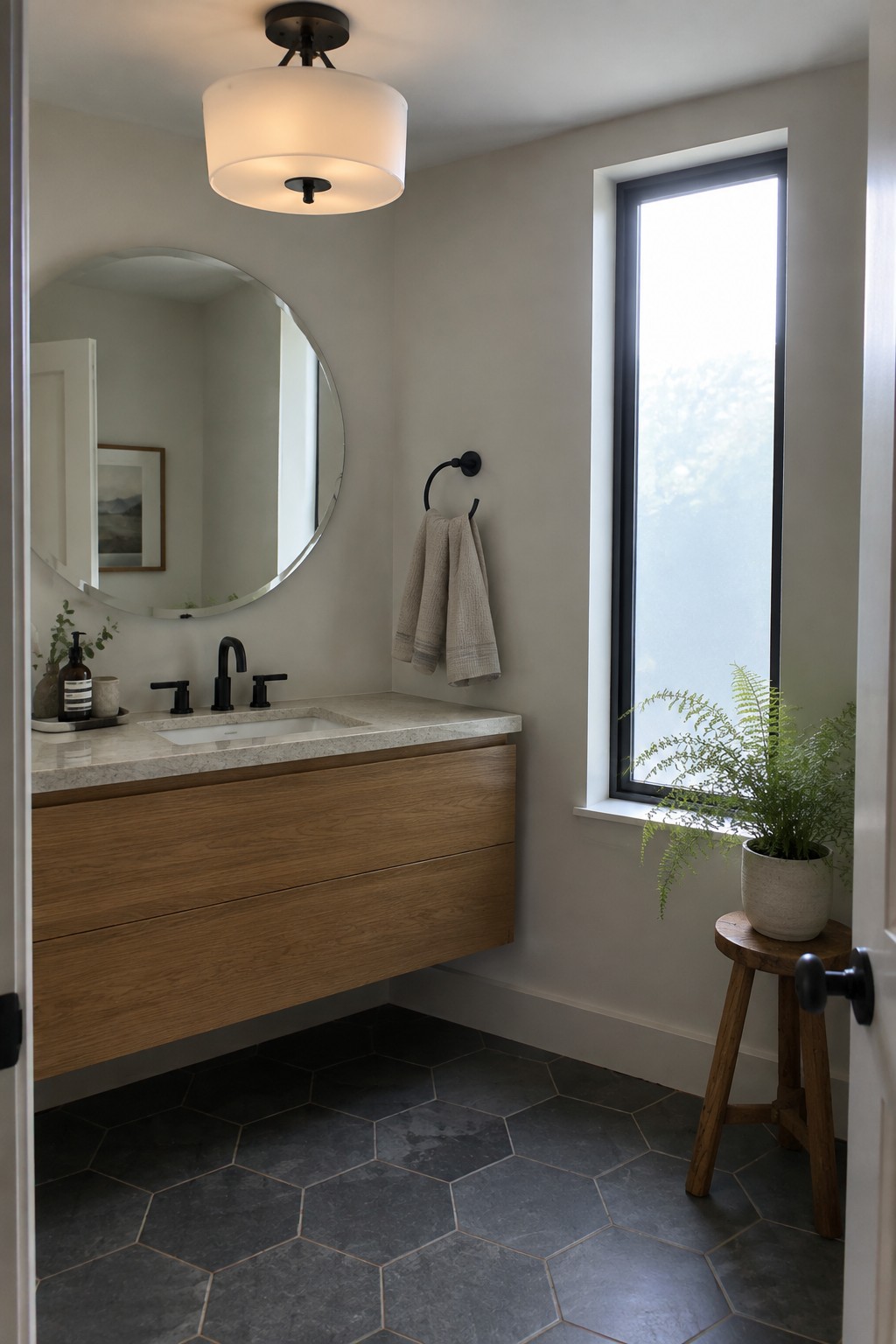 Modern bathroom with floating wood vanity, round mirror, black fixtures, and potted fern