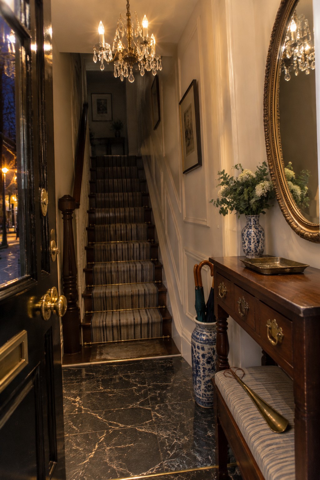Elegant hallway with striped staircase, crystal chandelier, marble floor, and wooden console