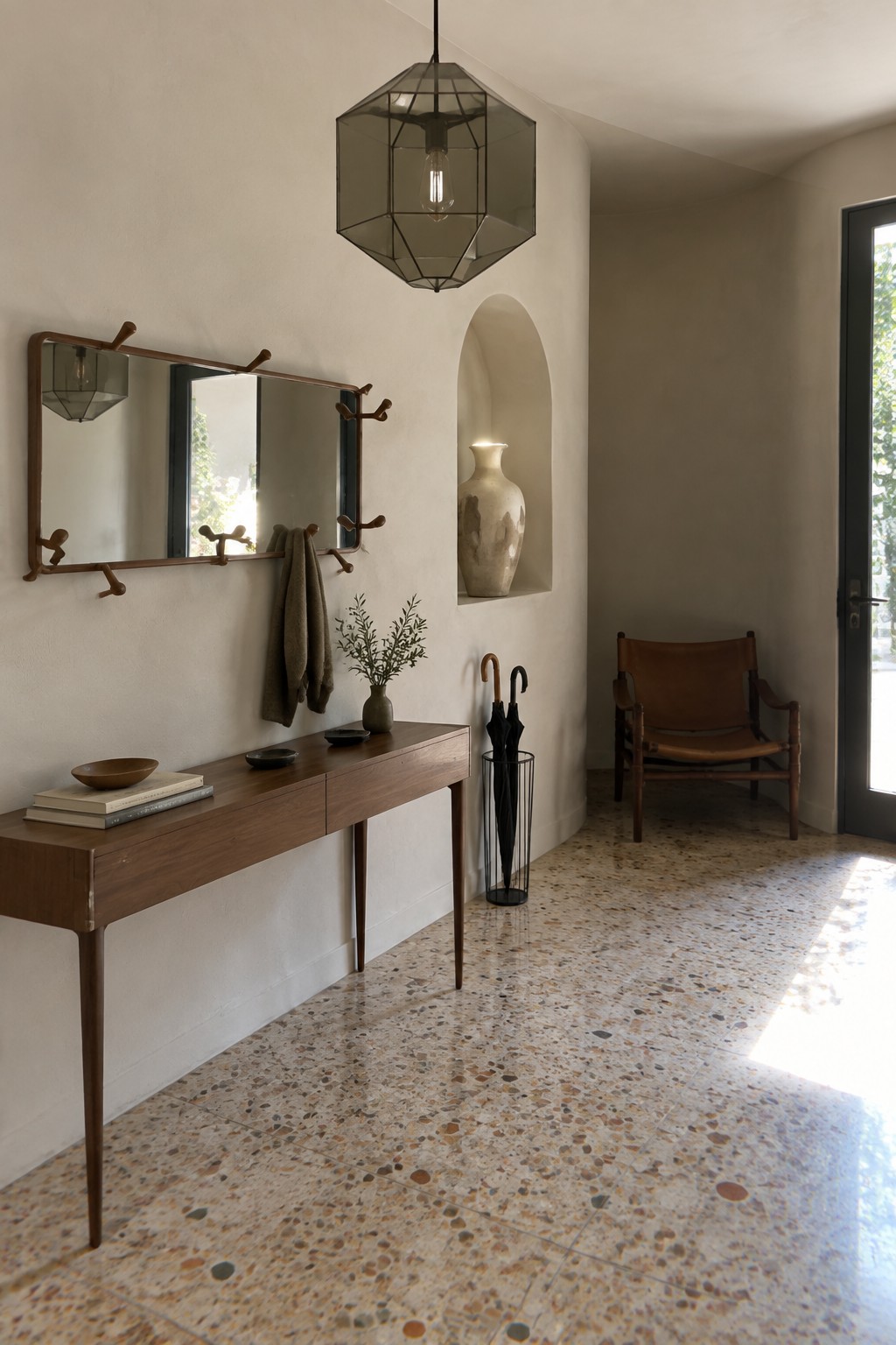 A minimalist foyer with a large geometric smoky glass lantern pendant hanging above a long wooden console table, a wall-mounted mirror, and a recessed niche holding a ceramic vase.
