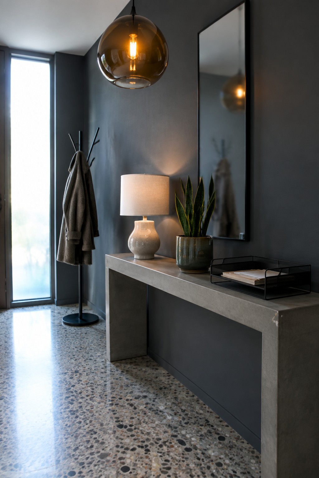 Modern entryway with concrete console, amber pendant light, snake plant, and coat rack.