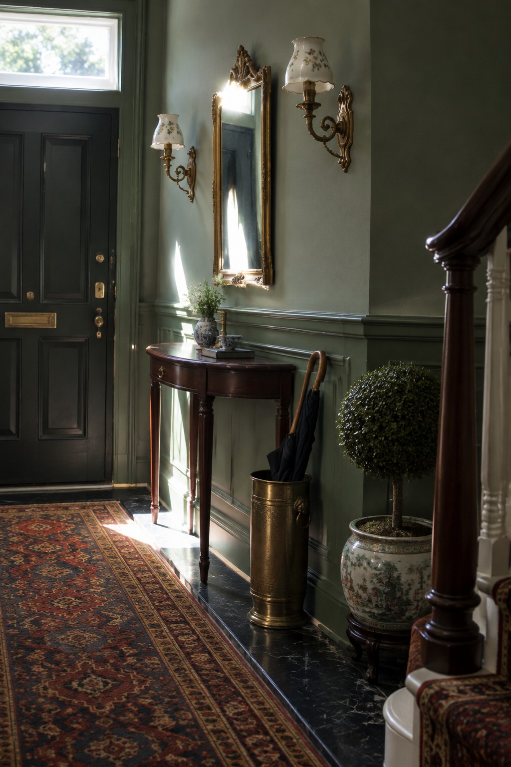 A narrow interior entryway with green walls shows two wall-mounted sconces flanking an ornate gold mirror above a dark wood console table.