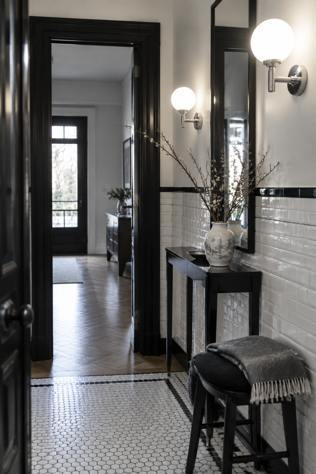 Elegant black and white hallway with console table, vase of branches, and stool