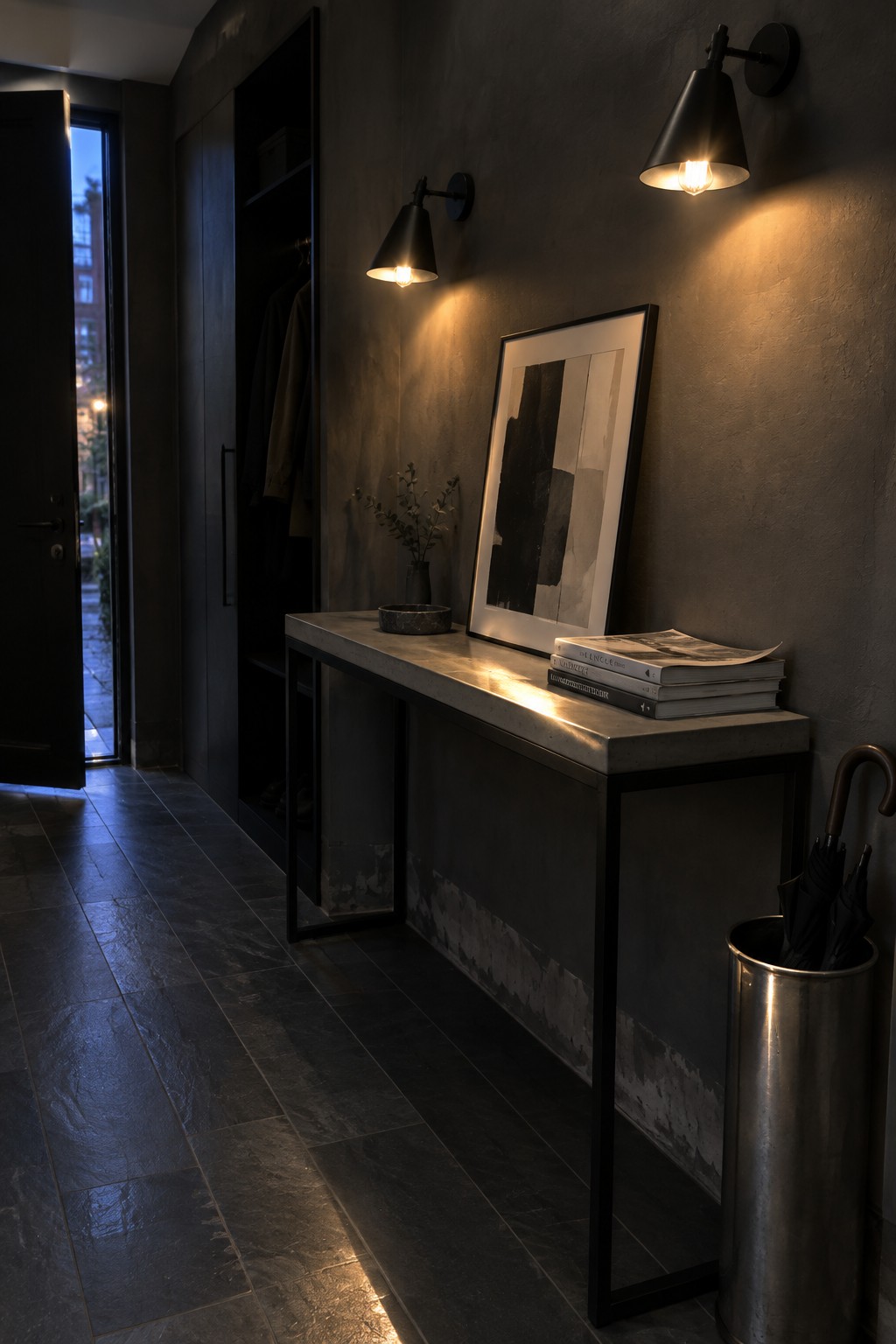 Dark entryway with concrete console, abstract art, wall sconces, books, and umbrella stand.