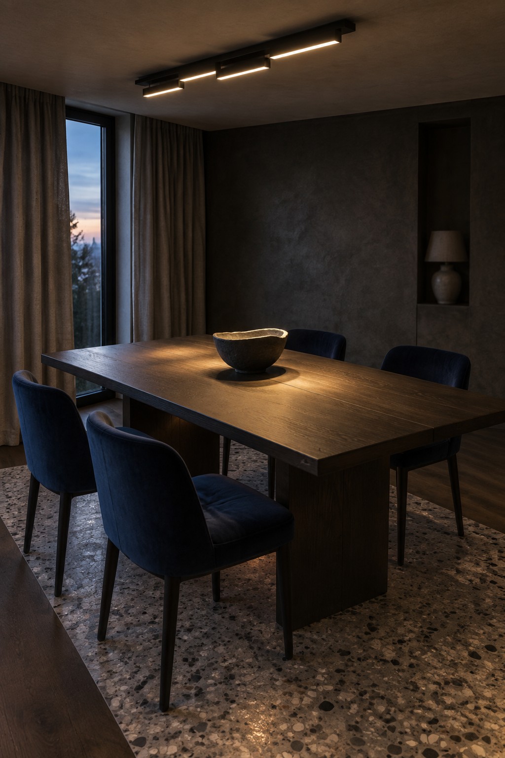 A dining room with a long wooden table, blue velvet chairs, and linear LED lights mounted on a dark ceiling.