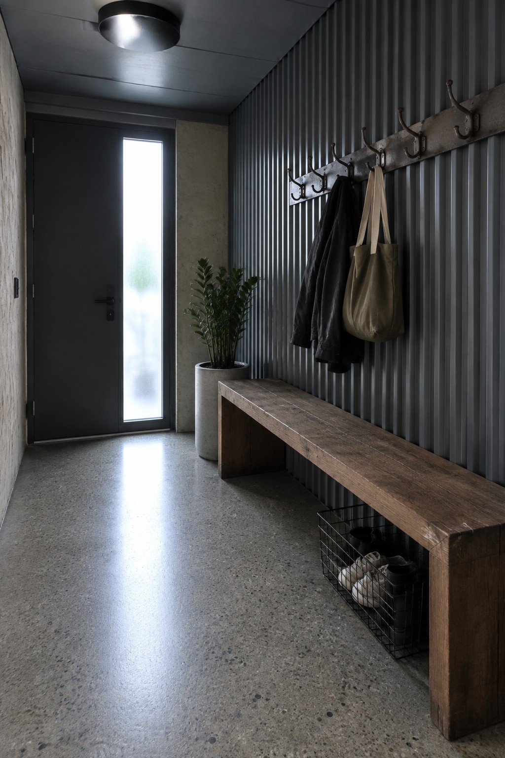 Modern entryway with wooden bench, coat hooks holding jacket and bag, potted plant.