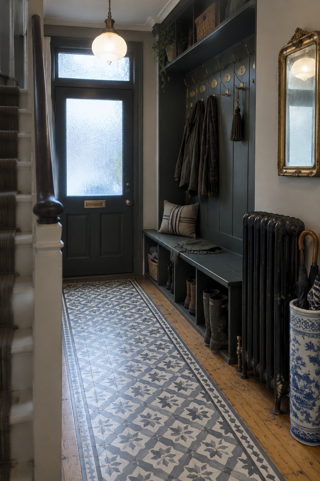 Dark green entryway with storage bench, hanging coats, boots, radiator, and patterned tile floor