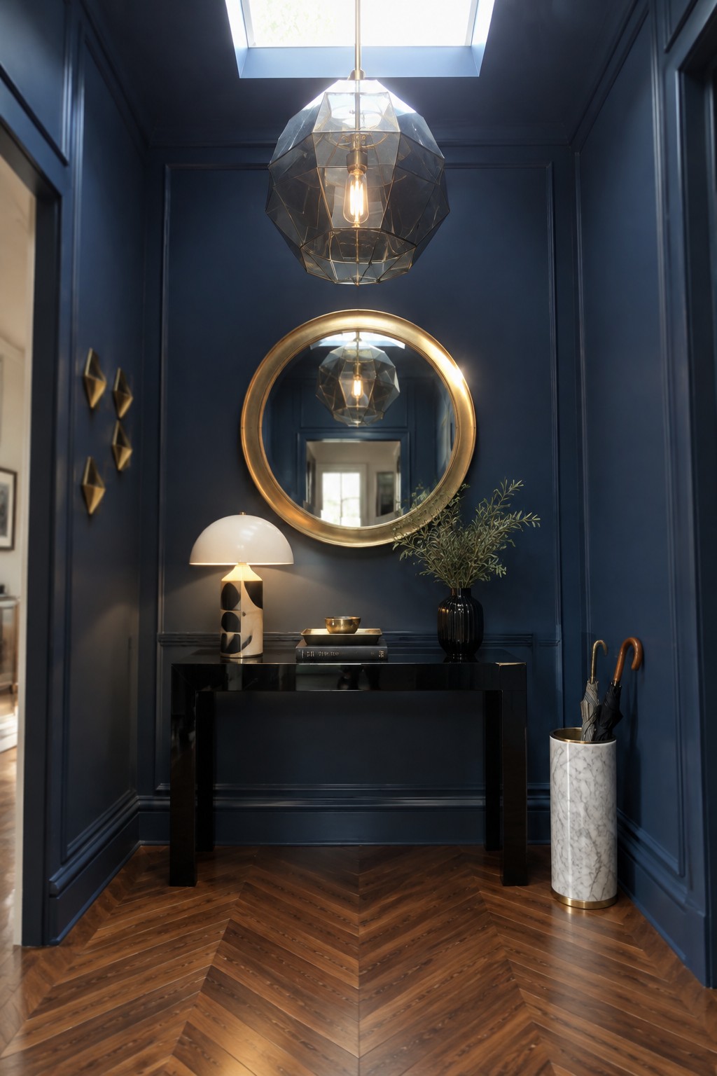 A large faceted geometric pendant light hanging from a skylight in a navy blue foyer above a black console table with a round gold mirror on the wall.
