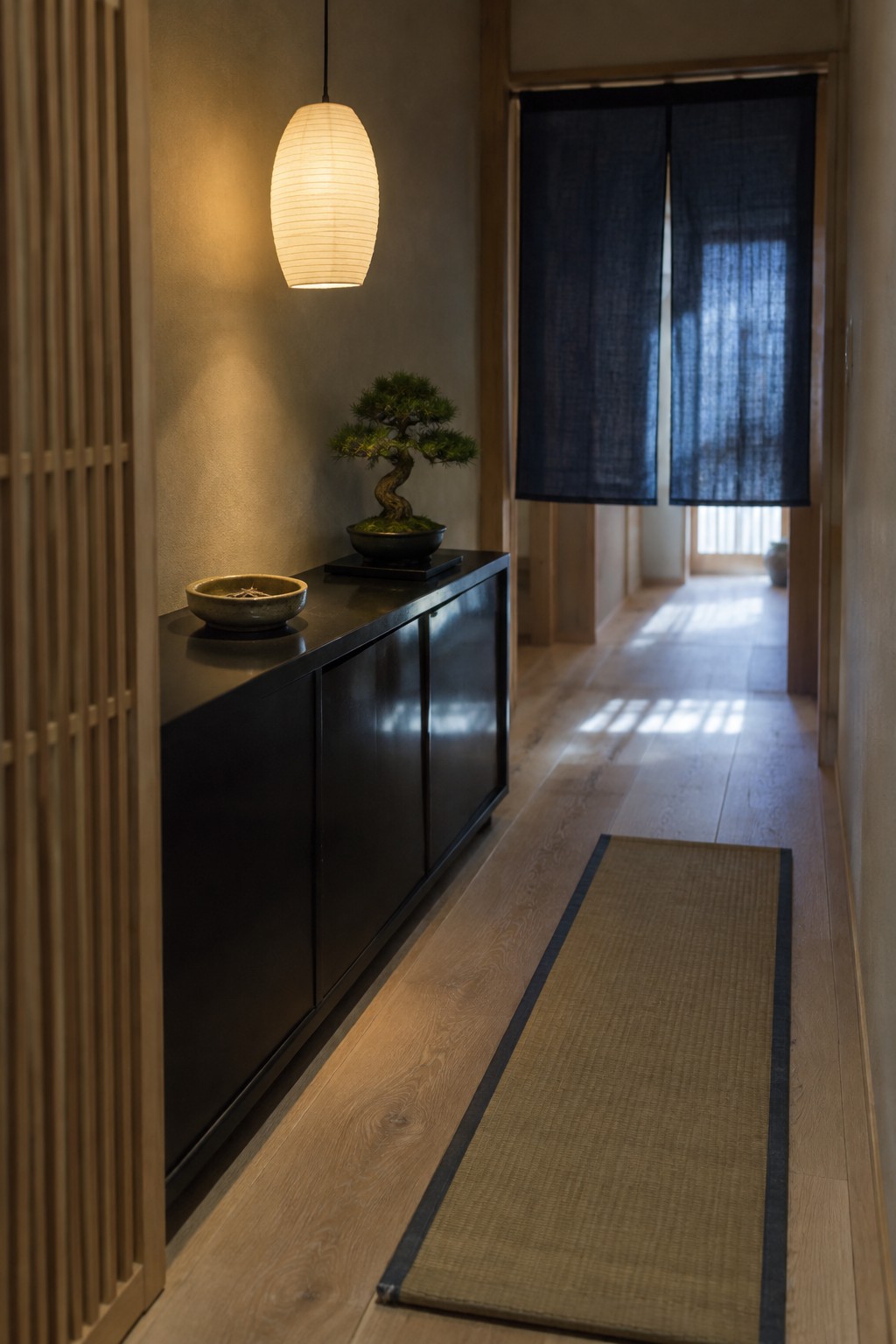 Traditional Japanese hallway with glowing lantern, bonsai on black cabinet, and woven runner
