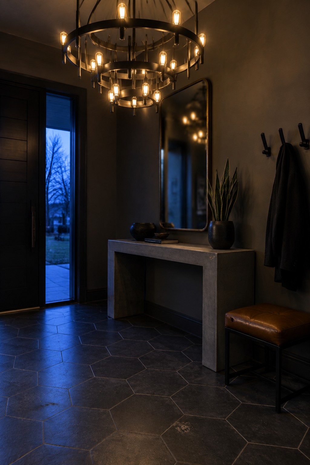 Modern entryway with glowing multi-ring chandelier, concrete console, mirror, and leather ottoman
