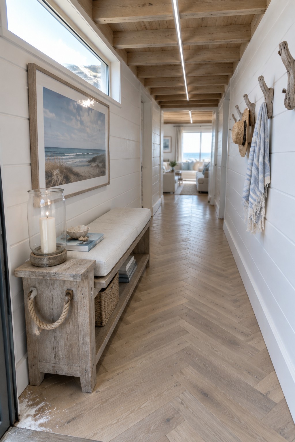 A narrow interior hallway with white shiplap walls, herringbone wood flooring, a light-colored bench, and one long linear ceiling light fixture running its length.