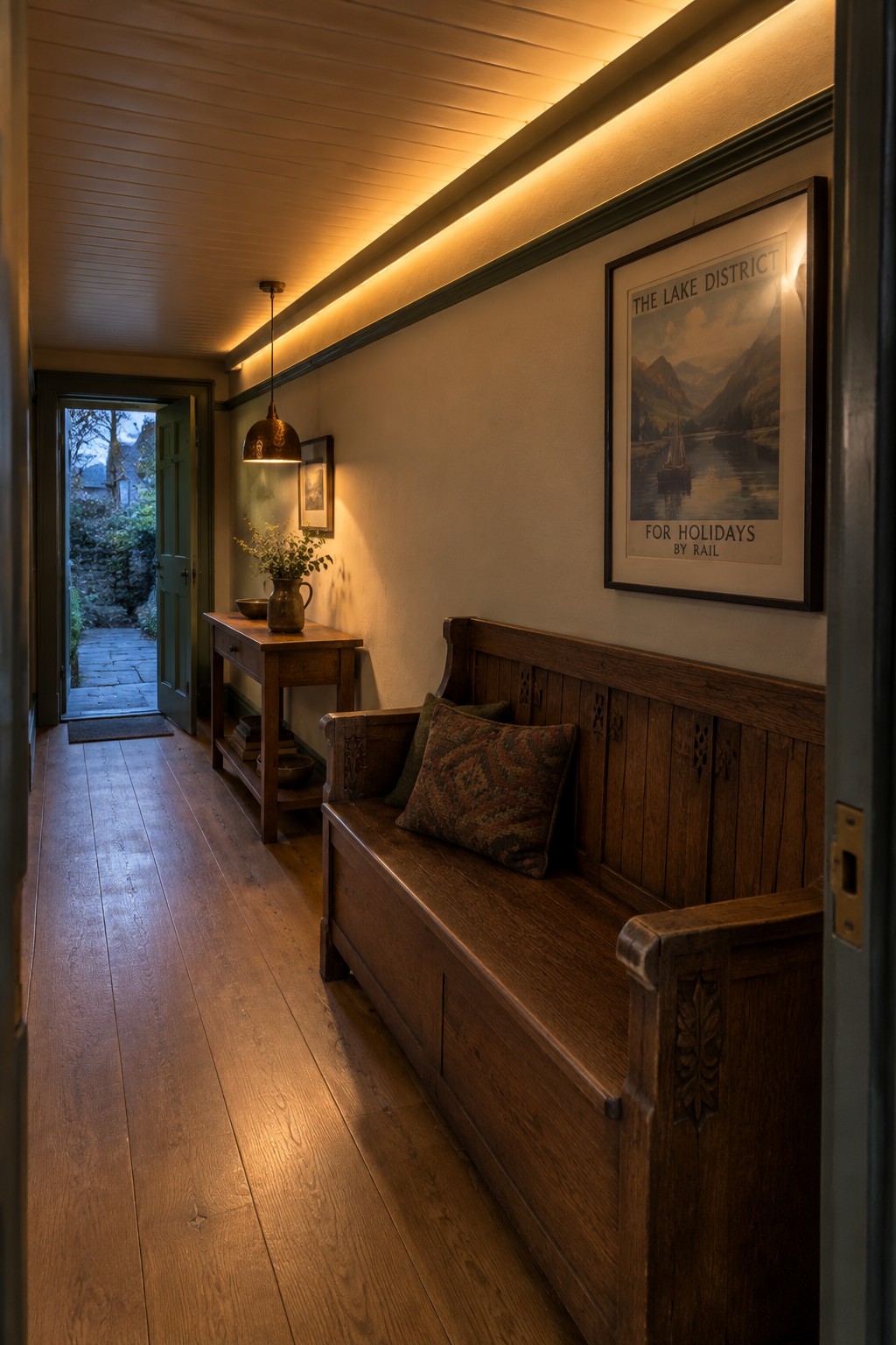 A narrow interior hallway with wood flooring, a long wooden bench with cushions, a console table, a framed poster on the wall, and linear lighting running along the upper wall and ceiling edge.